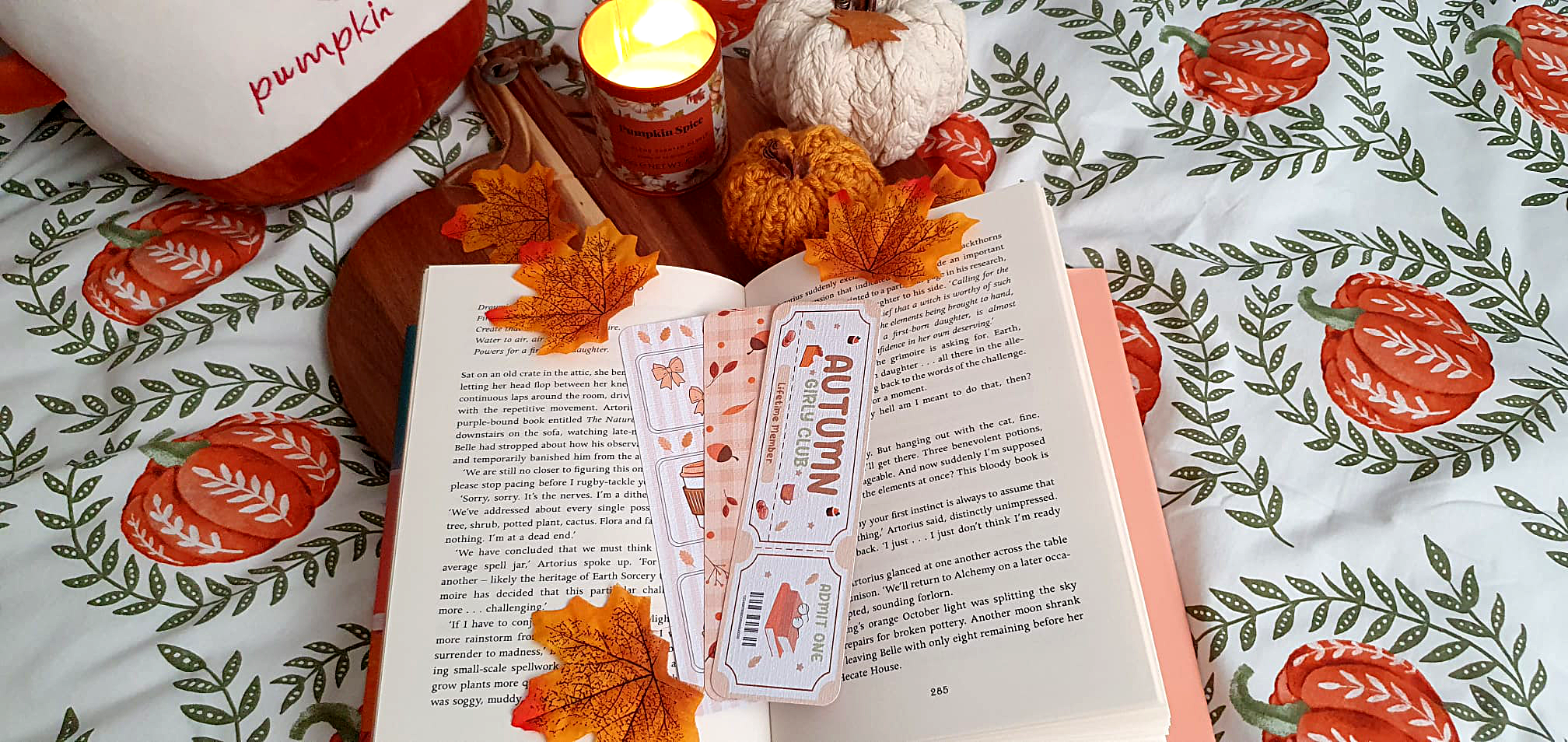 Open book with a candle and decorative pumpkins on a patterned fabric background